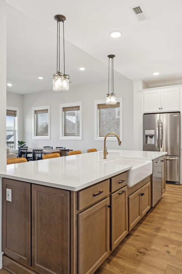 kitchen with a center island with sink, light wood-style flooring, appliances with stainless steel finishes, a sink, and recessed lighting