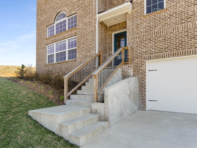 entrance to property with a garage, brick siding, and driveway