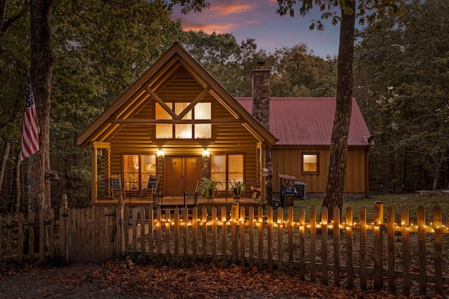 view of front of home featuring a fenced front yard, a chimney, metal roof, covered porch, and board and batten siding