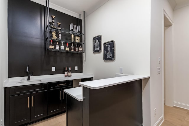 bar with light wood finished floors, wet bar, baseboards, and a sink