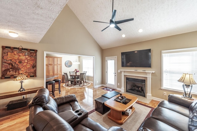 living area with light wood-style floors, a tile fireplace, a textured ceiling, and baseboards