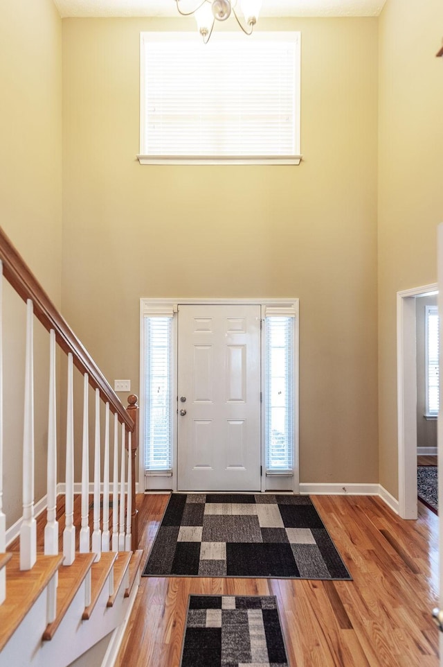 entrance foyer featuring stairway, a towering ceiling, an inviting chandelier, wood finished floors, and baseboards