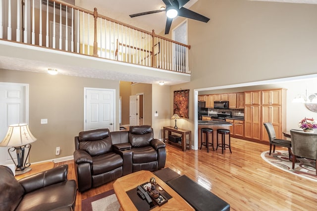 living area with ceiling fan, a high ceiling, light wood-type flooring, and baseboards