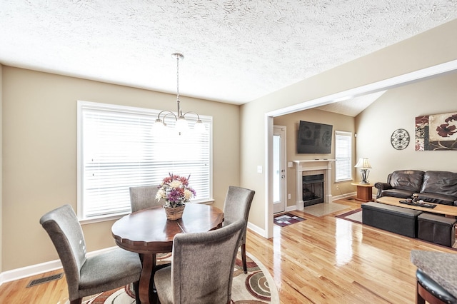 dining area featuring a fireplace, light wood finished floors, lofted ceiling, visible vents, and a textured ceiling