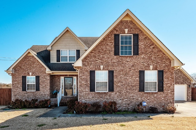 view of front facade with driveway, brick siding, roof with shingles, and fence