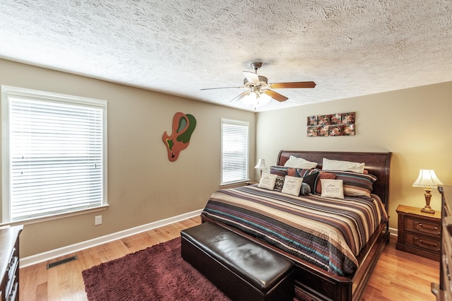 bedroom featuring baseboards, a textured ceiling, visible vents, and light wood-style floors