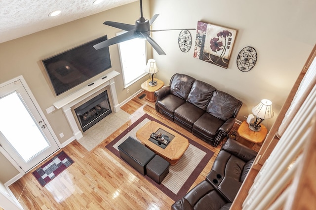 living room with a textured ceiling, ceiling fan, a fireplace, and wood finished floors