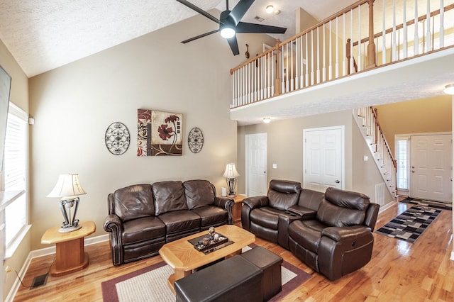 living area featuring ceiling fan, high vaulted ceiling, wood finished floors, baseboards, and stairway