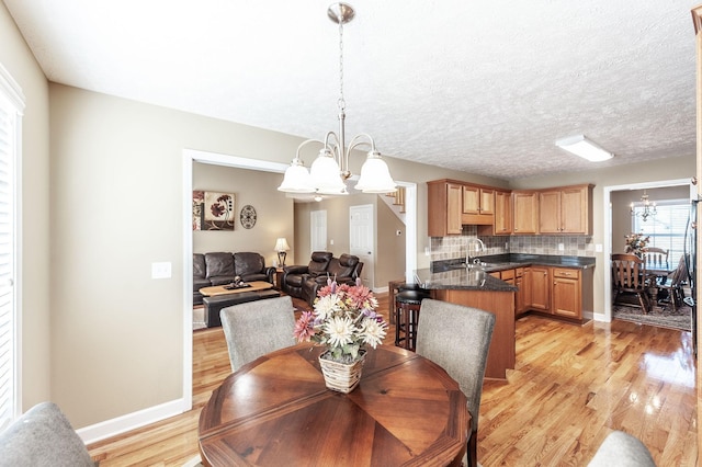 dining room with an inviting chandelier, baseboards, light wood finished floors, and a textured ceiling