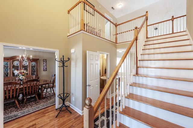 staircase featuring baseboards, visible vents, wood finished floors, a high ceiling, and a notable chandelier