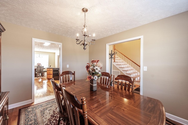 dining area featuring a textured ceiling, dark wood-type flooring, baseboards, and an inviting chandelier