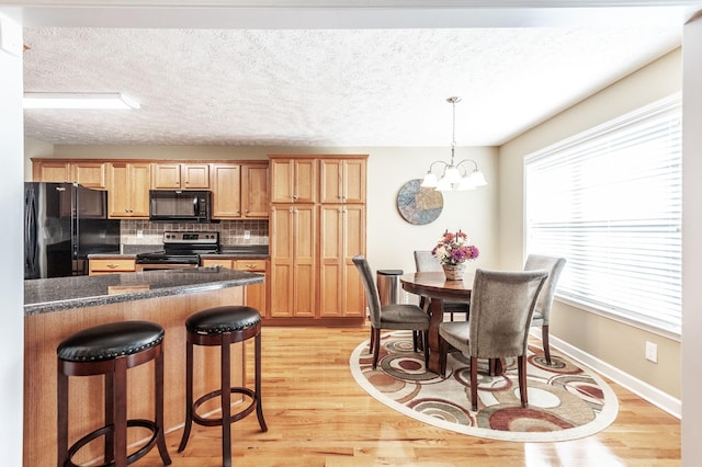 kitchen featuring light wood finished floors, dark countertops, backsplash, black appliances, and a kitchen bar