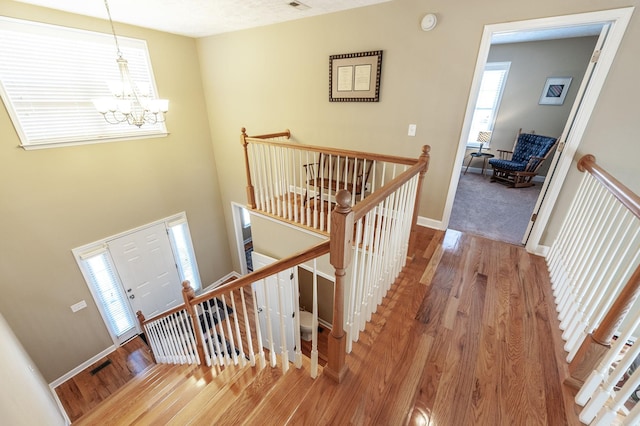 hall featuring baseboards, wood finished floors, an upstairs landing, and a notable chandelier