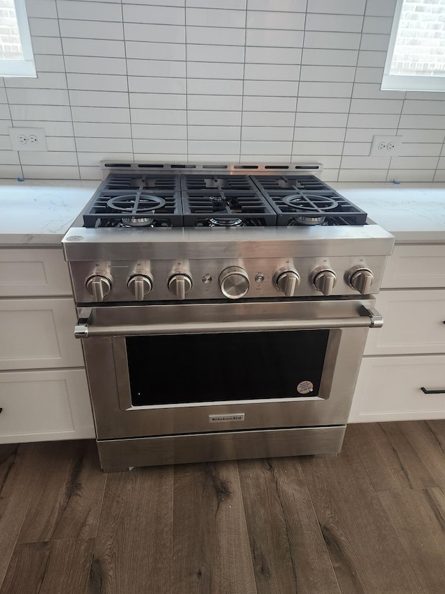 room details with stainless steel stove, dark wood-style flooring, white cabinetry, backsplash, and light stone countertops