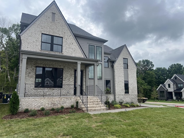 view of front of home featuring a front yard, covered porch, and brick siding