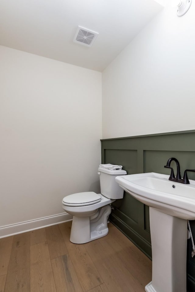 half bath with baseboards, visible vents, toilet, wood finished floors, and a sink