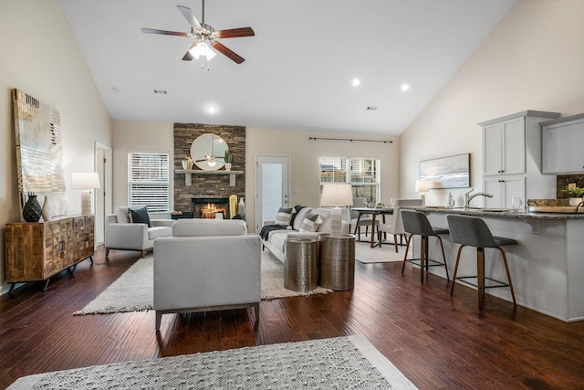 living area with dark wood-type flooring, high vaulted ceiling, a stone fireplace, and ceiling fan