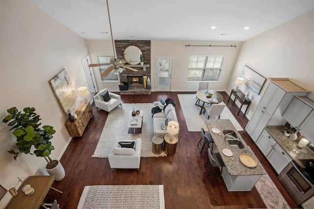 living room with a large fireplace, wood finished floors, a ceiling fan, and baseboards