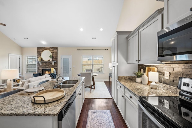 kitchen featuring decorative backsplash, dark wood finished floors, appliances with stainless steel finishes, light stone countertops, and a sink