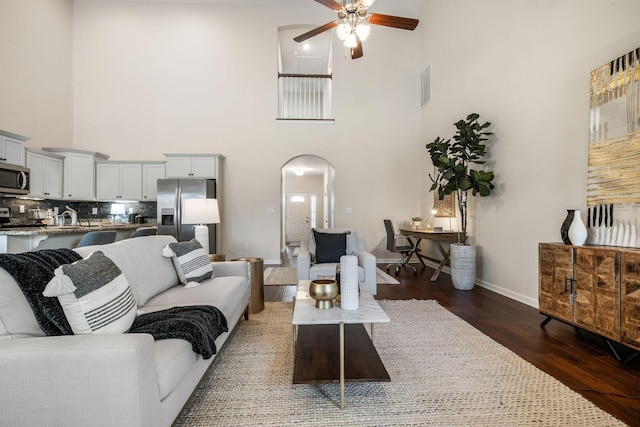 living room with arched walkways, visible vents, dark wood-type flooring, ceiling fan, and baseboards