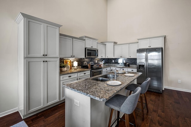 kitchen with stainless steel appliances, a sink, a kitchen breakfast bar, tasteful backsplash, and dark wood finished floors