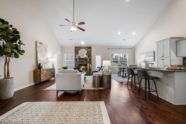 living area with dark wood-type flooring, a fireplace, high vaulted ceiling, and a ceiling fan