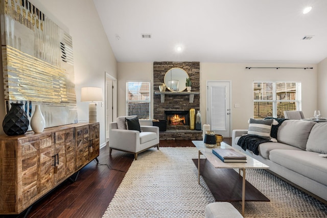 living area with vaulted ceiling, a stone fireplace, wood finished floors, and visible vents