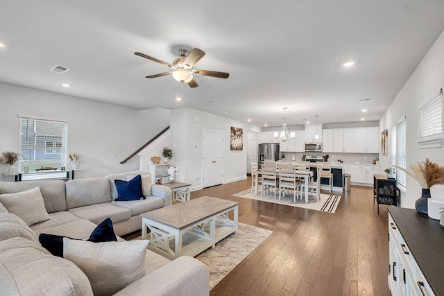 living room with visible vents, ceiling fan with notable chandelier, dark wood finished floors, and recessed lighting