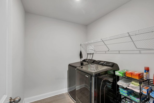 clothes washing area with washer and dryer, laundry area, baseboards, and wood finished floors