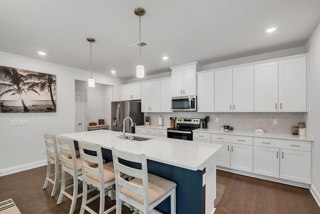 kitchen featuring stainless steel appliances, dark wood-style flooring, light countertops, backsplash, and a center island with sink