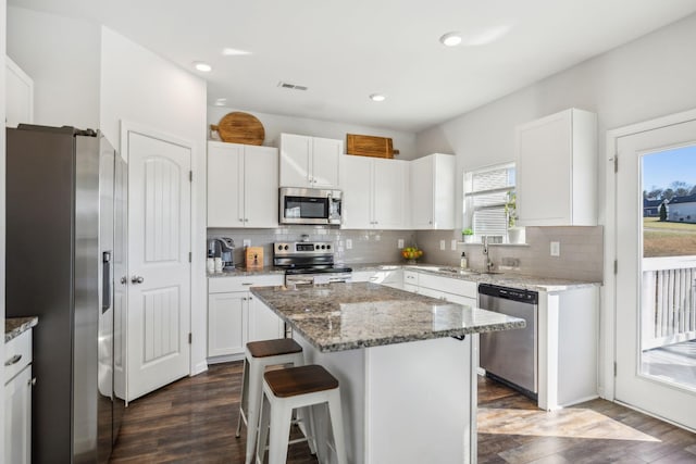 kitchen with appliances with stainless steel finishes, white cabinets, a sink, a kitchen island, and a kitchen breakfast bar