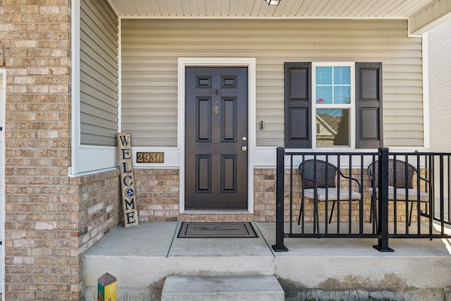 view of exterior entry featuring covered porch and brick siding