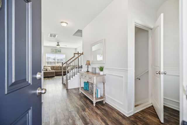 entryway with a decorative wall, a wainscoted wall, visible vents, stairs, and dark wood finished floors