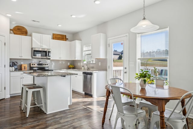 kitchen featuring dark wood-style floors, stainless steel appliances, tasteful backsplash, white cabinets, and a kitchen island