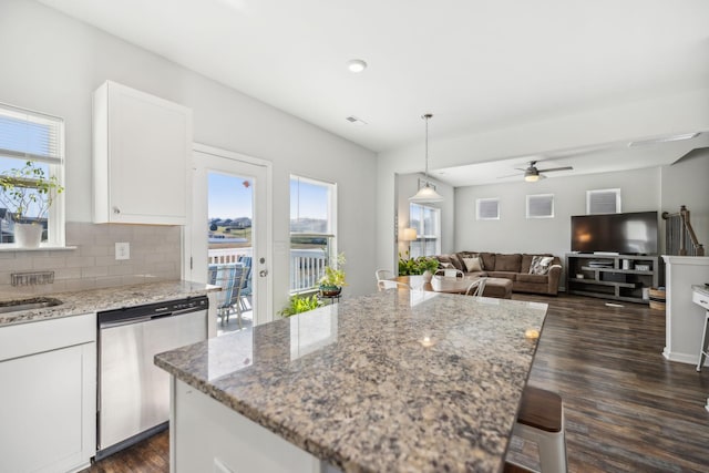 kitchen featuring dark wood-style flooring, white cabinets, stainless steel dishwasher, light stone countertops, and tasteful backsplash