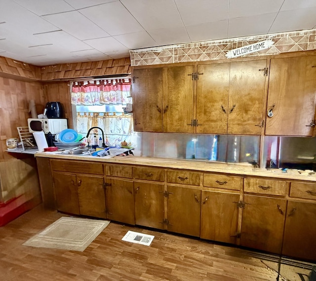 kitchen with a sink, visible vents, light countertops, light wood finished floors, and brown cabinetry