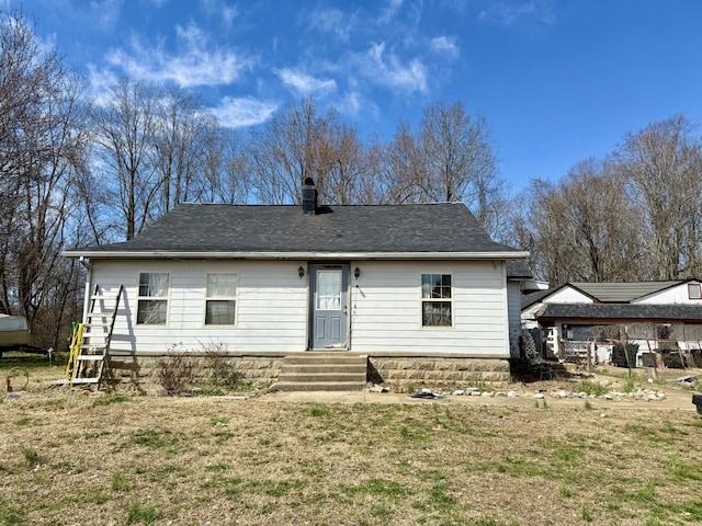 rear view of house featuring a shingled roof, entry steps, a yard, and a chimney