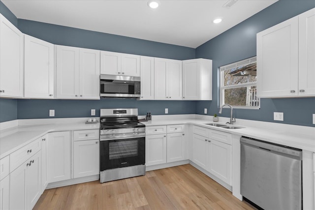 kitchen with light wood finished floors, white cabinets, appliances with stainless steel finishes, light countertops, and a sink