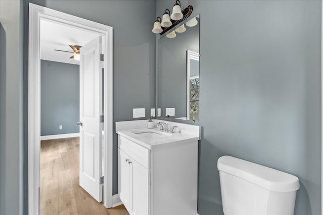 half bathroom featuring toilet, baseboards, wood finished floors, and vanity