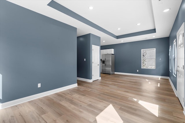 empty room featuring light wood-type flooring, baseboards, a raised ceiling, and recessed lighting