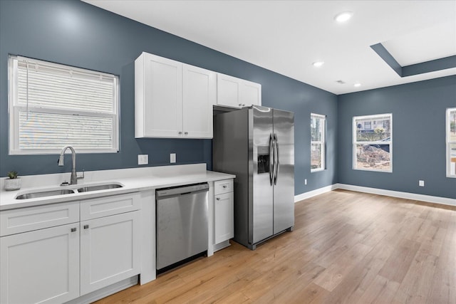 kitchen featuring stainless steel appliances, light countertops, light wood-style floors, white cabinetry, and a sink