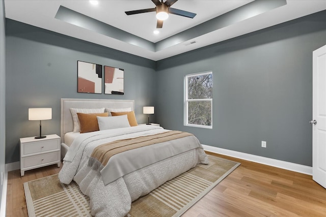 bedroom featuring baseboards, wood finished floors, visible vents, and a raised ceiling