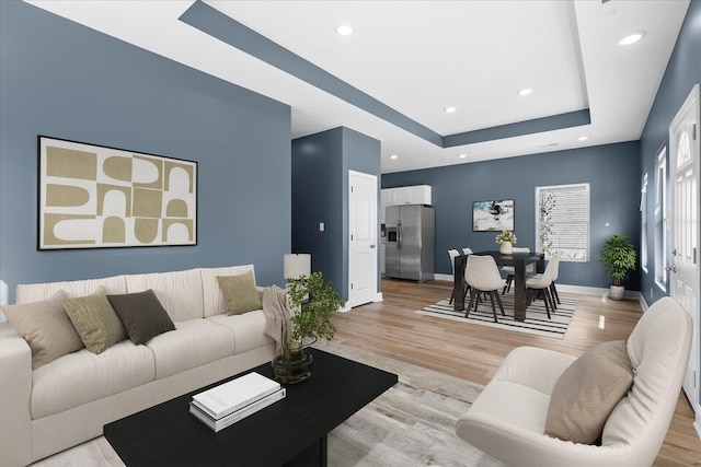 living room with a tray ceiling, light wood-style floors, baseboards, and recessed lighting