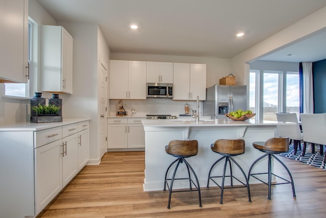 kitchen featuring light wood finished floors, stainless steel appliances, light countertops, white cabinets, and a kitchen bar