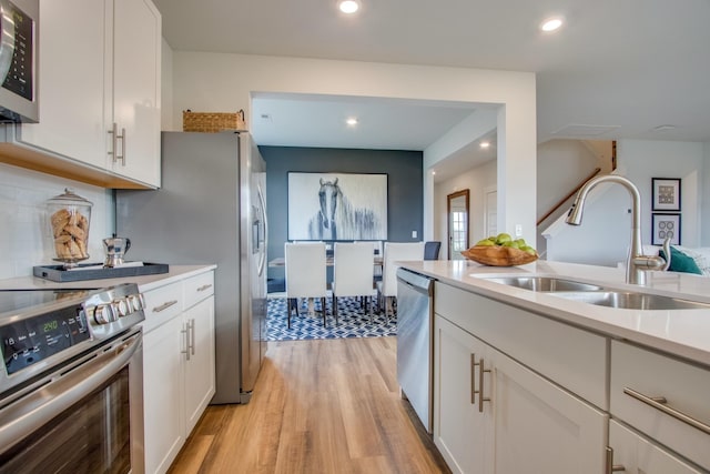 kitchen with light wood finished floors, stainless steel appliances, light countertops, white cabinets, and a sink