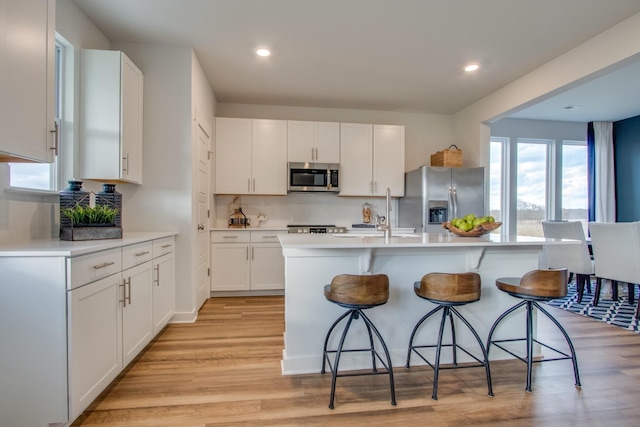 kitchen with white cabinets, light wood-style flooring, stainless steel appliances, light countertops, and a kitchen bar