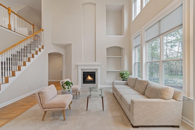 living area with built in shelves, baseboards, stairway, light wood finished floors, and a glass covered fireplace