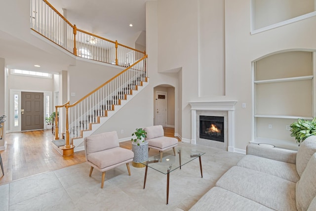 living area featuring a towering ceiling, stairway, a glass covered fireplace, wood finished floors, and baseboards