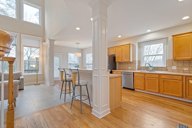 kitchen featuring a sink, decorative columns, light countertops, and stainless steel dishwasher