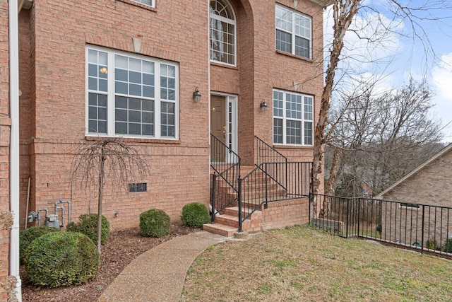 entrance to property with a yard, crawl space, brick siding, and fence